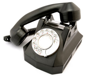 Photo of an old black rotary phone with the receiver off the hook.